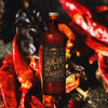 Fire-roasted chiles in the backdrop. In the foreground, a bottle of Ancho Reyes Barrica Chile Ancho Liqueur.