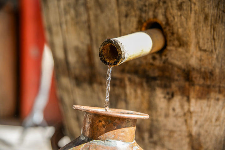 Water flowing from a bamboo spout into a ceramic container against a wooden background