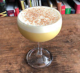 Cocktail with a frothy top in a glass on a wooden surface with books in the background