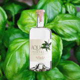 Bottle of Aqua Perfecta Basil Eau de Vie over backdrop of green plant.