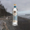A bottle of Astraea Ocean Gin positioned in front of a beach background, emphasizing the oceanic theme of the spirit.