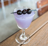 Purple cocktail with three cherries on a wooden surface