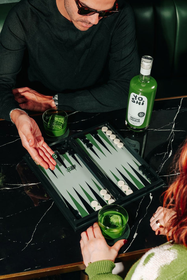Two people playing backgammon with green bottles on a table