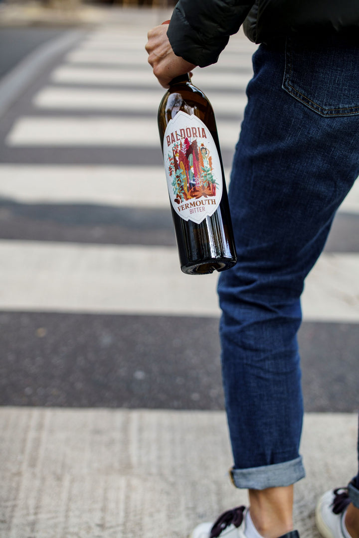 Person holding a bottle with a colorful label on a street crossing.
