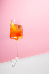 Wine glass with orange liquid on a pink background