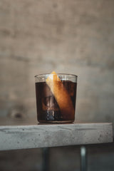 Glass of dark liquid with a lemon twist on a concrete surface against a blurred background