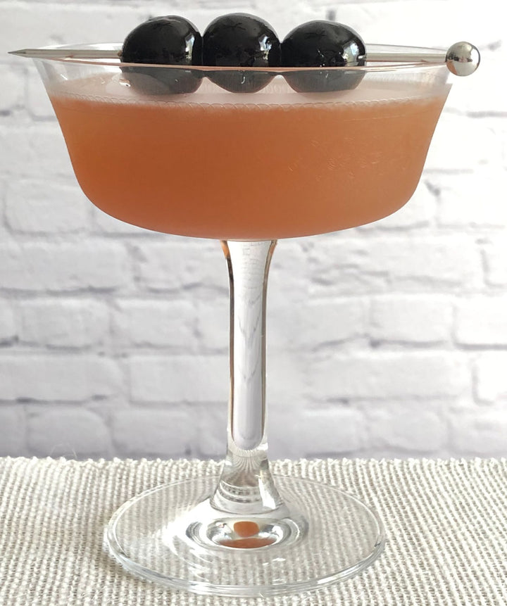 Cocktail in a coupe glass with black olives on a white brick wall background