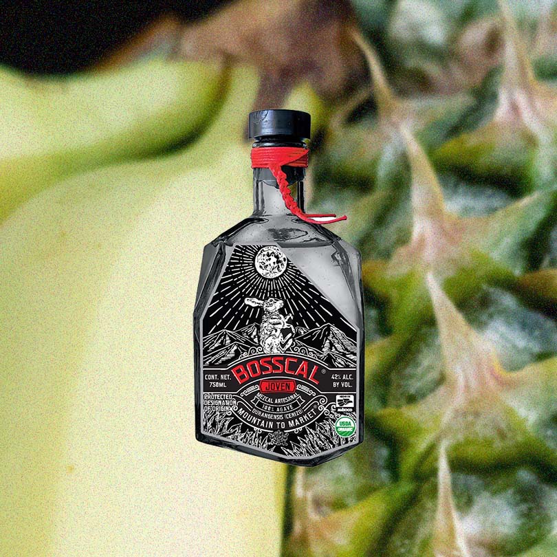 Bottle of Mezcal Bosscal Joven over backdrop of green fruit.