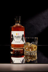 Coconut Cartel bottle of rum with a glass of rum on a dark surface
