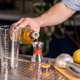 Person pouring liquid from a bottle into a measuring glass on a bar counter.