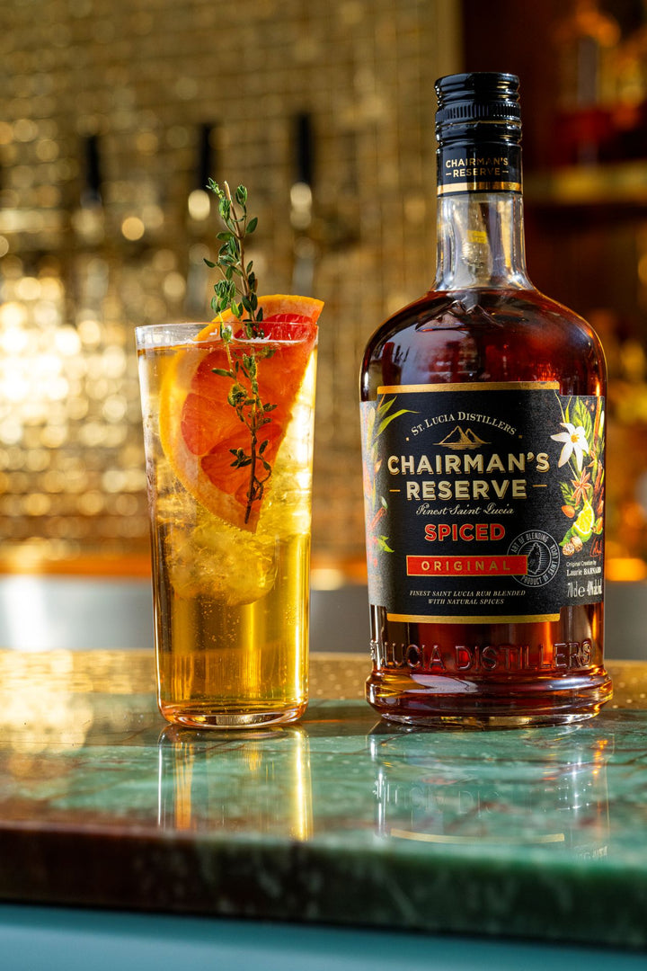Bottle of Chairman's Reserve Spiced Rum on a table next to a high ball cocktail.
