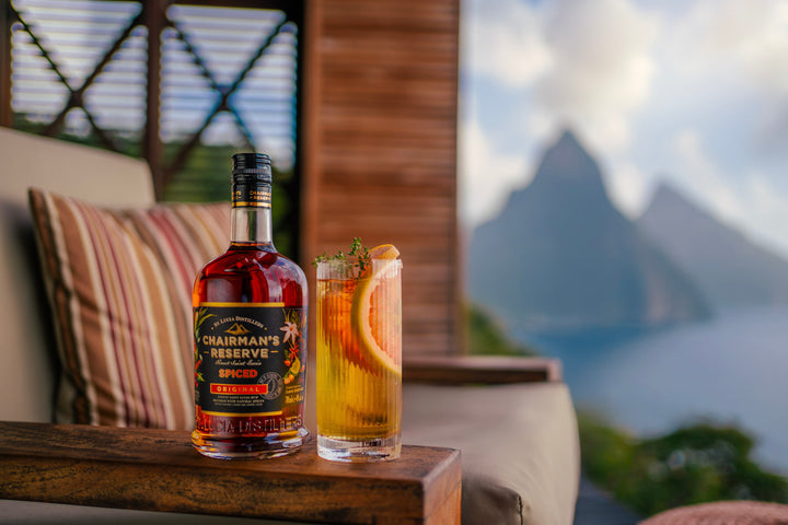 Bottle of Chairman's Reserve Spiced Rum behind a high ball cocktail outdoors.