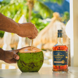 Person pouring Chairman's Reserve rum into a coconut with a tropical setting in the background
