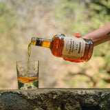 Person pouring Chairman's Reserve Rum into a glass with a blurred natural background