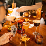 People playing cards with drinks and snacks on a wooden table