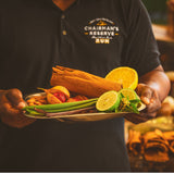 Person holding a plate of spices and citrus fruits with 'Chairman's Reserve Rum' logo in the background