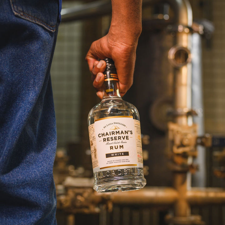 Hand holding a bottle of Chairman's Reserve Rum in front of a distillery background