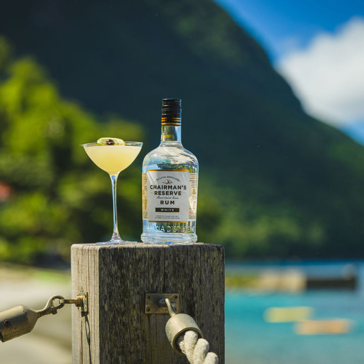 Bottle of Chairman's Reserve Rum with a cocktail on a wooden post against a scenic background