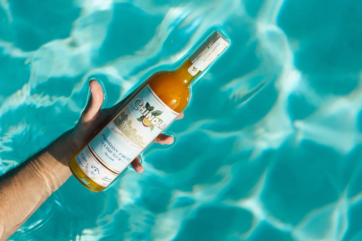 Hand holding a bottle of orange juice with a pool in the background