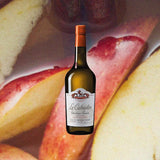 A yellow-hued glass bottle with an orange foil covering.  It looks not dissimilar to a wine bottle. The label is similar too, it reads: Le Calvados de Christian Drouin.  The label has lion illustration at the top and the whole thing is set against what looks like the backdrop of a great french manor house.  This is against a backdrop of a close-up of seasoned apple slices resting in their own juices in pleasing colors of red and yellow.