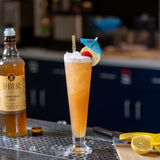 Cocktail with lemon garnish and bottle of Liberon Cinnamon Syrup on a bar counter.