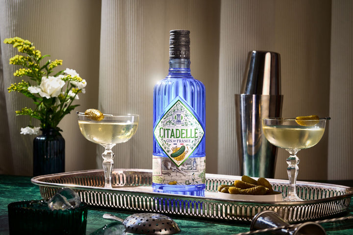 Bottle of Citadelle gin on a tray with cocktails and flowers in the background