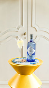 Citadelle gin bottle on a yellow stool with a decorative coaster and glass in a stylish interior setting.