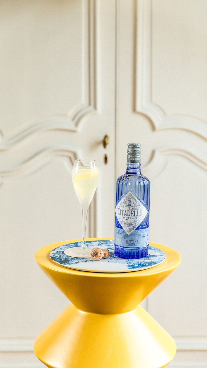 Citadelle gin bottle on a yellow stool with a decorative coaster and glass in a stylish interior setting.