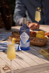 Citadelle gin bottle on a wooden table with drinks and snacks