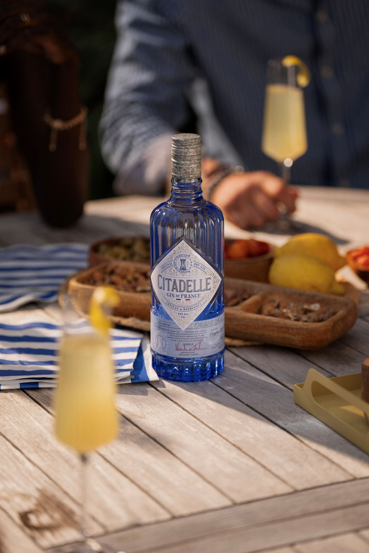 Citadelle gin bottle on a wooden table with drinks and snacks