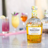 Bottle of Clément Bana Canne liqueur on a bar counter with cocktails in the background