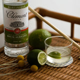 Bottle of Clément rhum agricole with a glass of rum and lime on a woven surface.