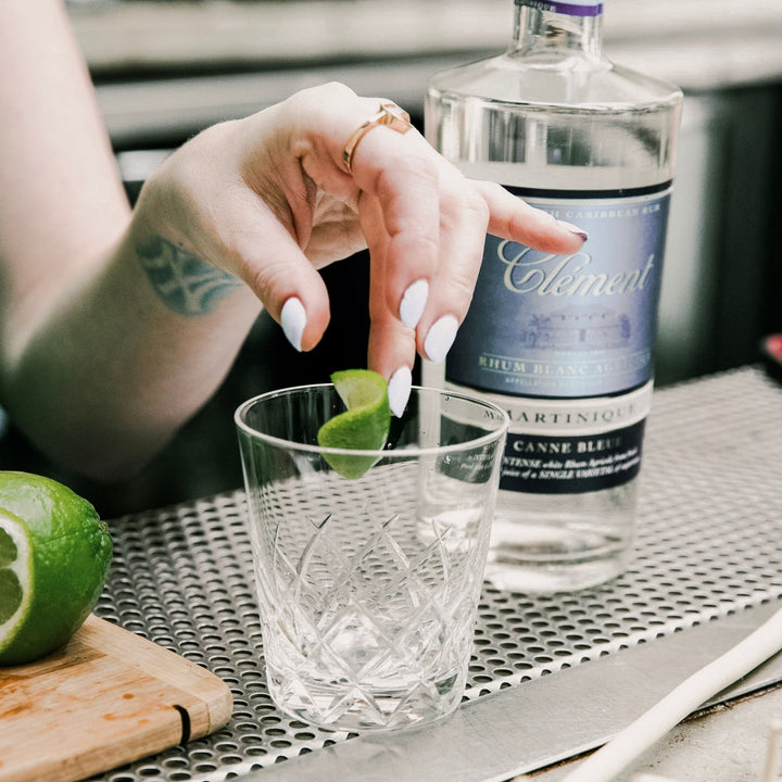 Person preparing a cocktail with a bottle of Célèment rum in the background.