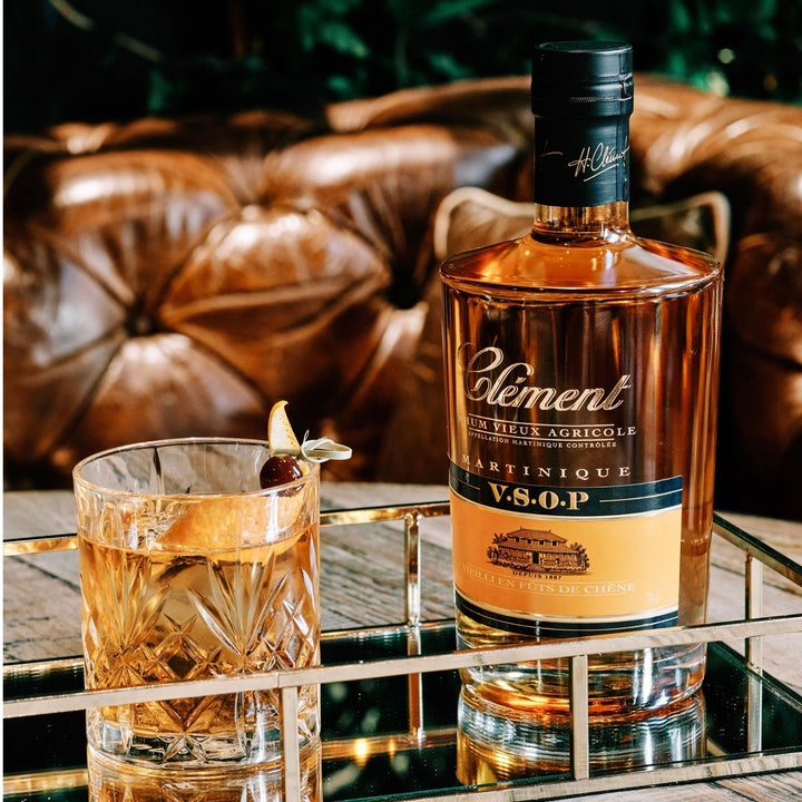 Bottle of H. Clement Martinique V.S.O.P. cognac with a glass on a reflective surface.