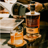 Bottle of Clément rum with a glass of rum on a wooden coaster, blurred background
