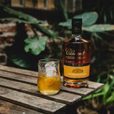 Bottle of Clément rhum vieux agricole and a glass of cocktail on a wooden surface with greenery in the background