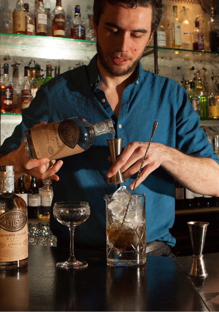 Barista preparing a cocktail with bottles and glasses in the background