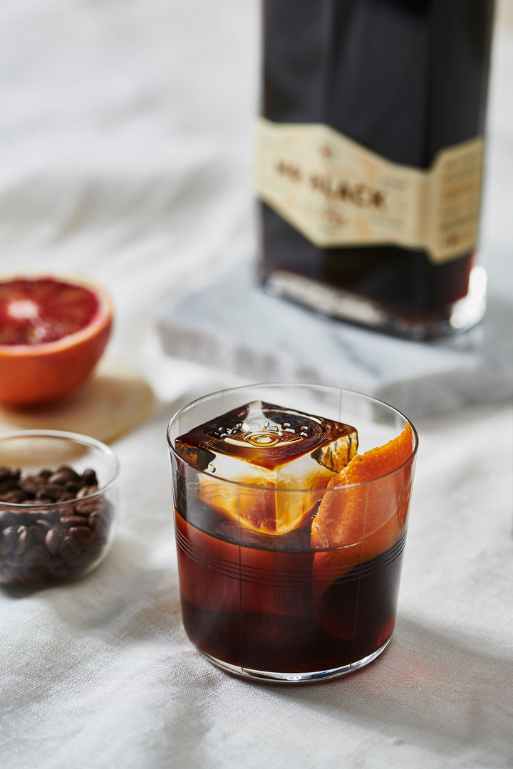 Glass of iced coffee with blood orange slices, coffee beans, and a coffee bag on a light surface.