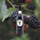 Bottle of Combier Crème de Mûre Blackberry Liqueur over back drop image of black berries.