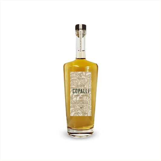 An elegant looking bottle of caramel colored liquid with a label that reads Copalli Barrel Rested Rum against a backdrop of illustrated rainforest flora and fauna.