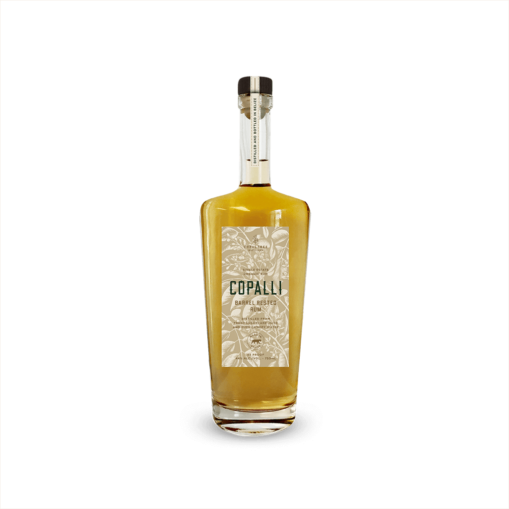 An elegant looking bottle of caramel colored liquid with a label that reads Copalli Barrel Rested Rum against a backdrop of illustrated rainforest flora and fauna.