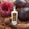 A tall elegant bottle of clear rum with a label that reads Copalli Cacao Single Estate Organic. The label, rich browns and reds, depicts cacao leaves and beans in illustration.  All against a macro shot of beries in delicious chocolate with chocolate shavings, evoking the taste of the rum.