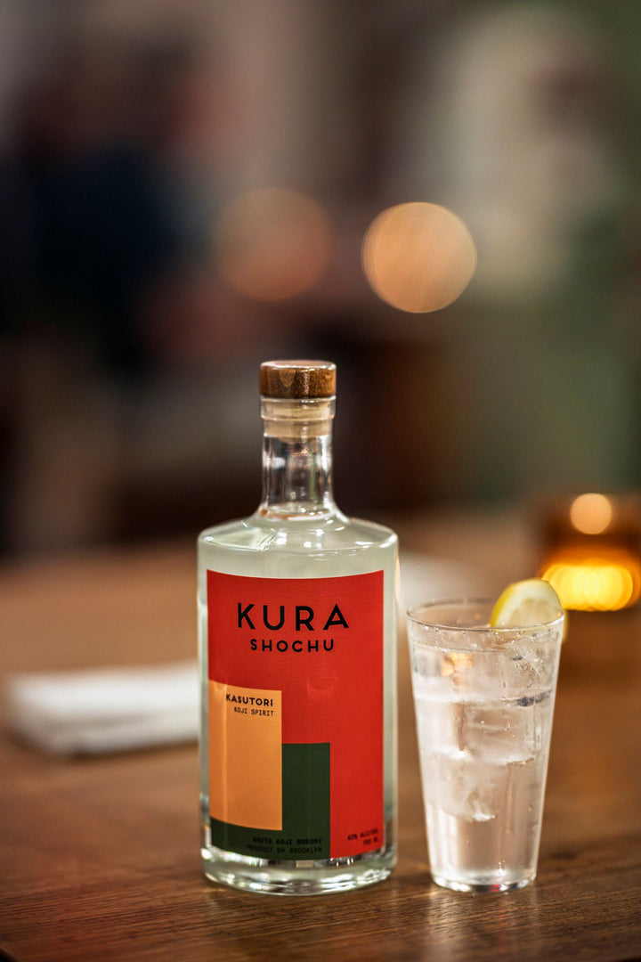 Kura Shochu bottle with a glass of water on a wooden table