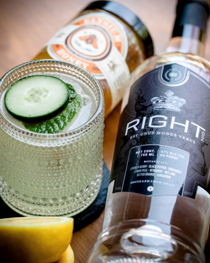 Bottle of 'Right' gin with a cocktail garnished with cucumber and lemon on a wooden surface.