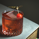 Basil smash cocktail on a table with a cherry garnish.