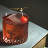 Basil smash cocktail on a table with a cherry garnish.