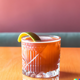 Red cocktail on a table in the style of a contemporary cocktail recipe book.