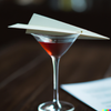 Paper Plane cocktail with a paper plane garnish sitting on a table.