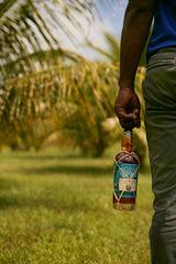 Person holding a bottle of Planteray Cut & Dry in a grassy outdoor setting with palm trees.