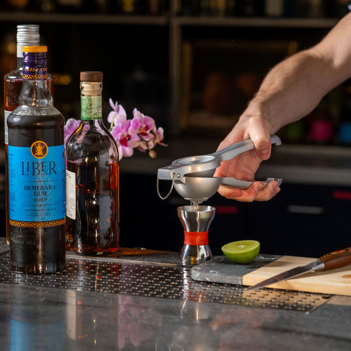 Bartender preparing a cocktail with Liber Demerara Syrup and other ingredients on a bar.